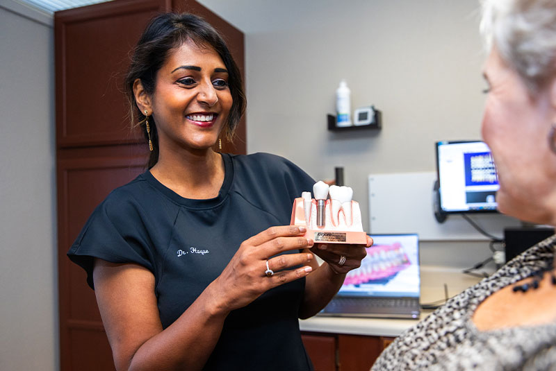 Doctor holding up model of dental implants to sow Patient